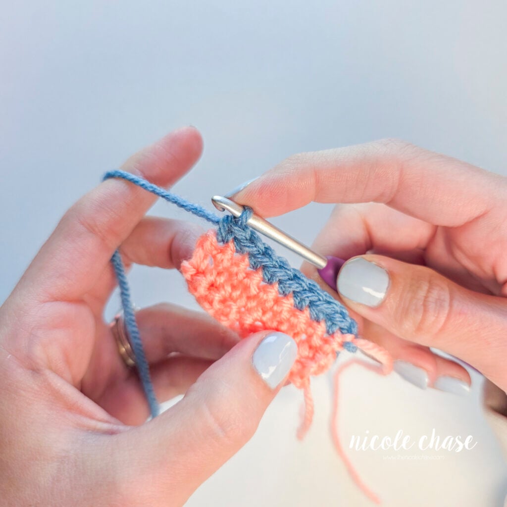 A row of blue single crochet stitches have been worked across the top of a pink crochet swatch.