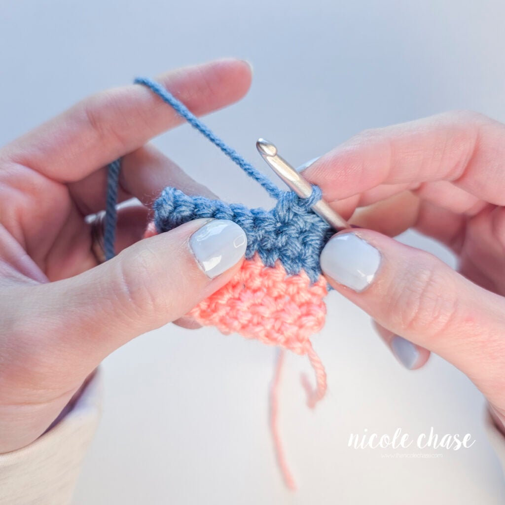 Crochet swatch in pink and blue yarn, held by two hands.