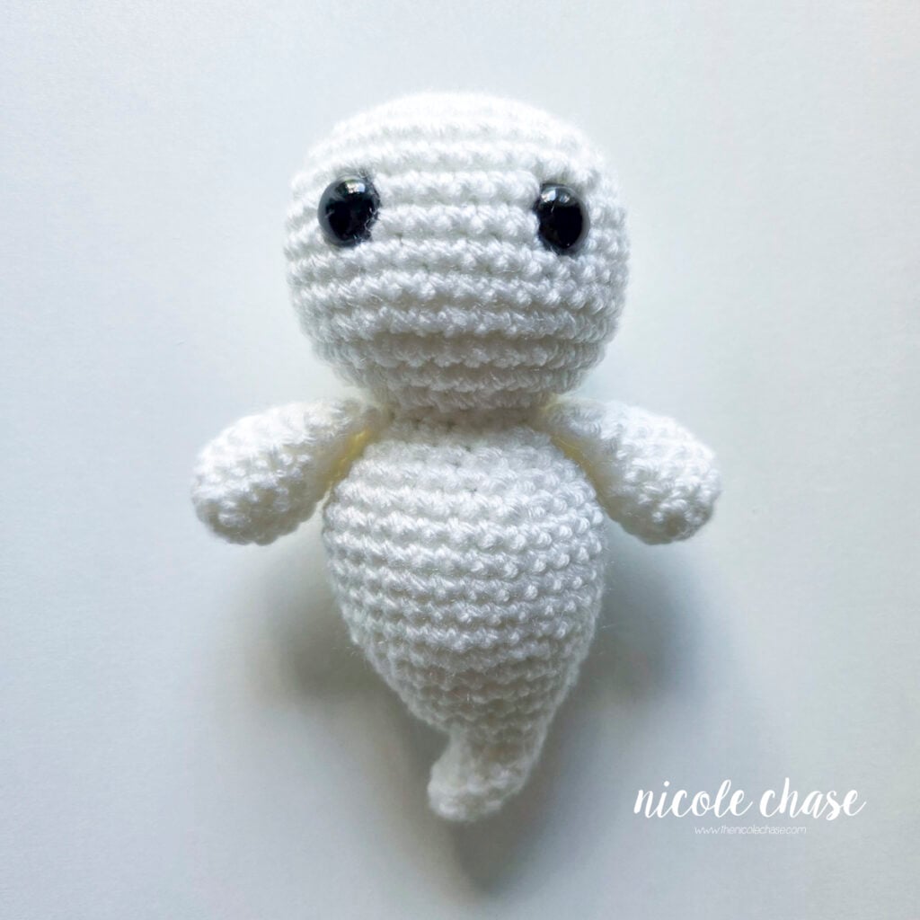 Crocheting the ghost is completed with the head being finished and closed shut, and the black safety eyes are in place.