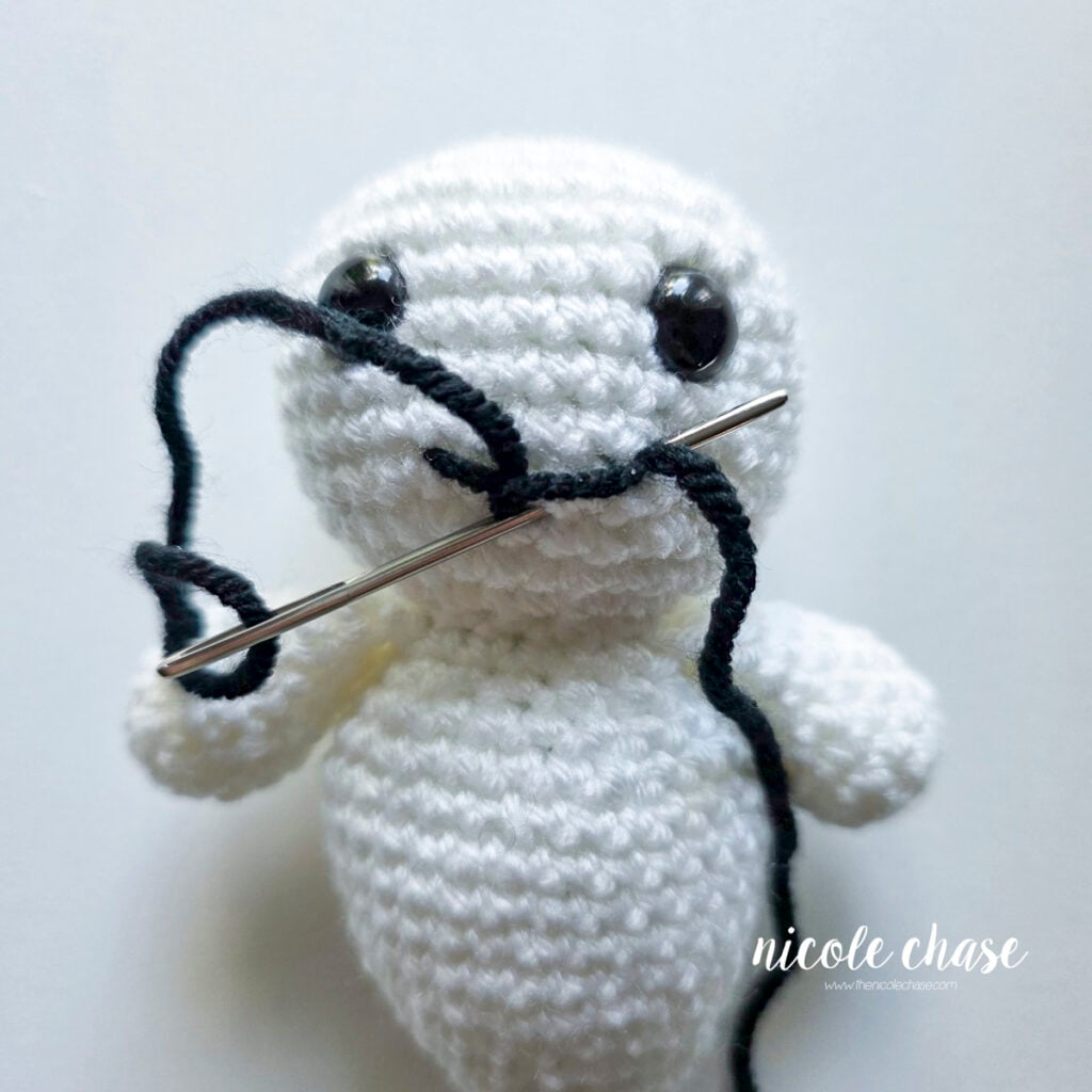 The black yarn has been looped around over the line, and the yarn needle is now being pushed back to the starting position.