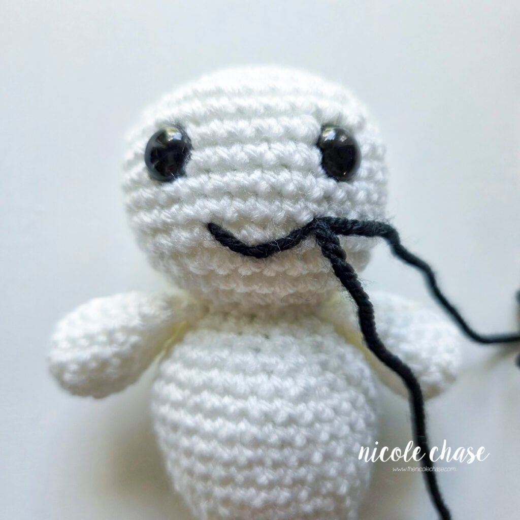 The smile is complete and the black yarn tails remain on the right side of the smile on the ghost plush.