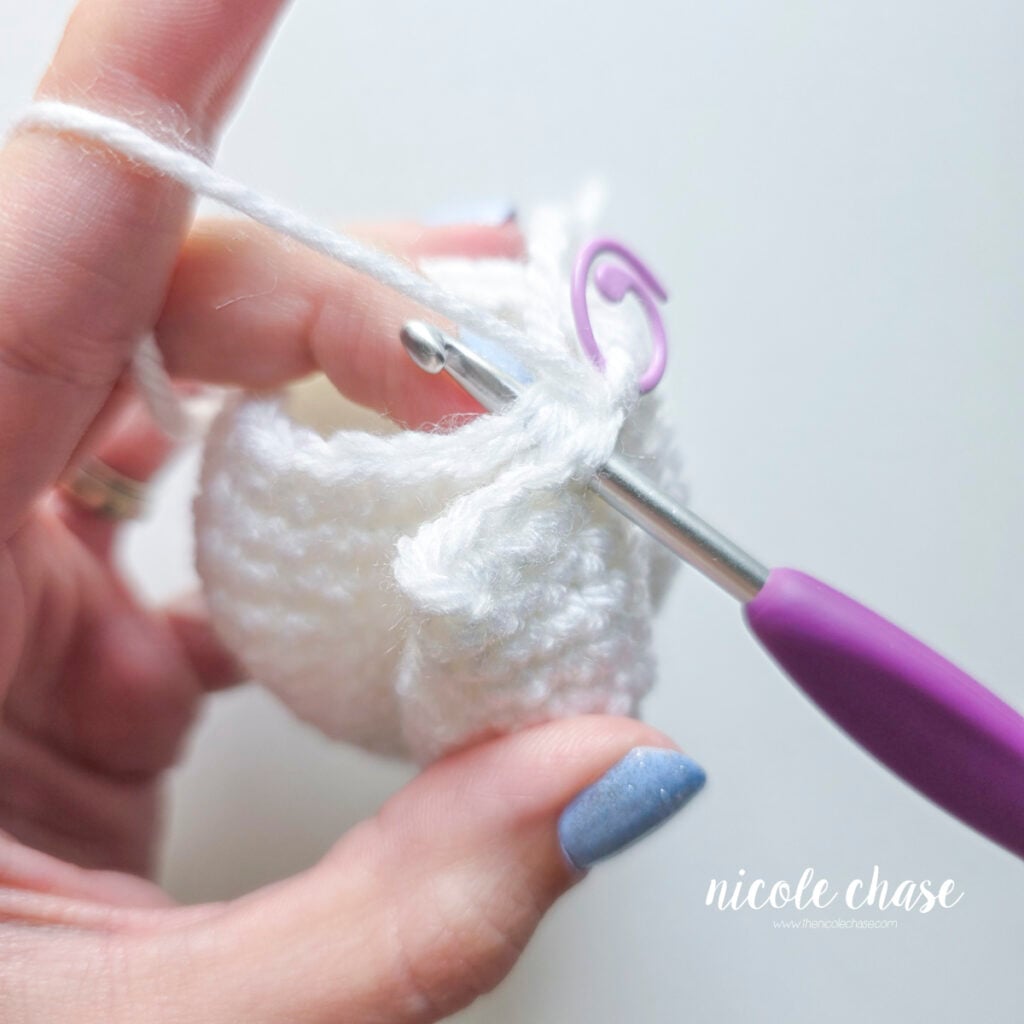 Inserting the crochet hook between the first arm and the body of the ghost to begin crocheting them together.