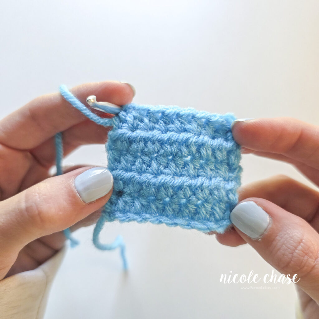 Hands holding a completed swatch of the half double crochet stitch showing straight edges and visible row texture. 