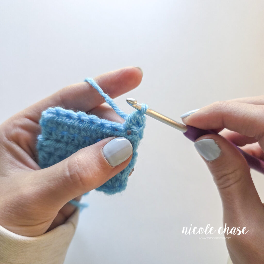 Completed half double crochet stitch on a blue swatch with one loop now remaining on the hook. 