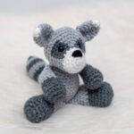 Finished amigurumi raccoon plushie made form a free raccoon crochet pattern sitting on white faux fur.