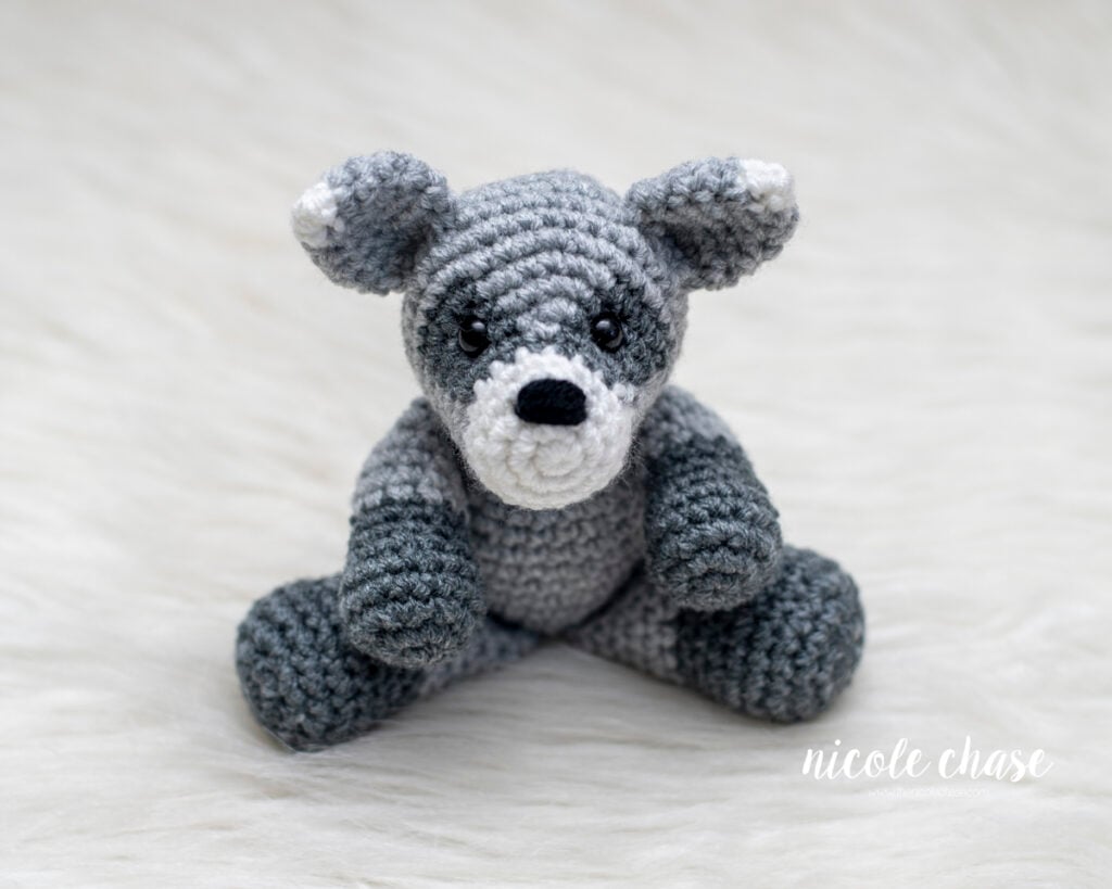 Front view of a completed crochet raccoon amigurumi sitting on a white fur surface.