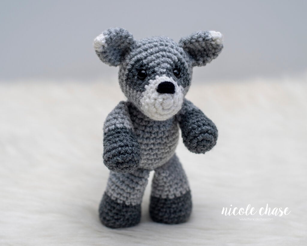 Standing crochet raccoon plushie displaying full body construction, dark gray paws, and white-tipped ears.