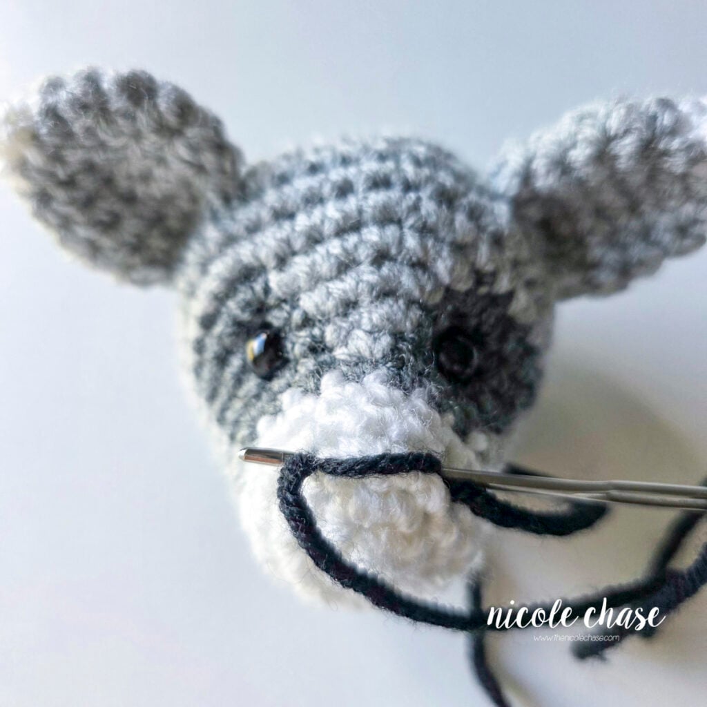 Continue wrapping the black yarn around the front of the head to create the embroidered nose on the crochet raccoon. 