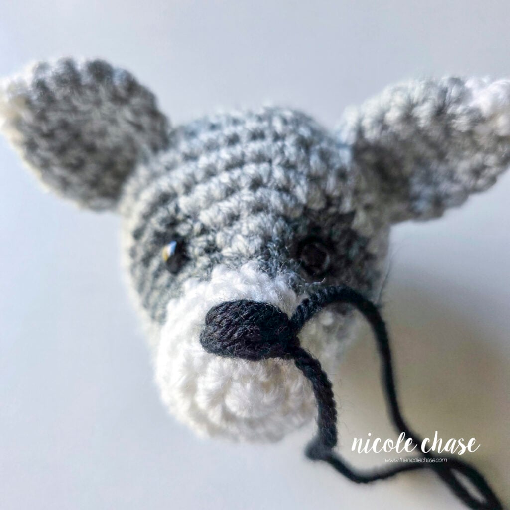 The embroidered nose on the crochet raccoon has been completed with the yarn tails remaining. 