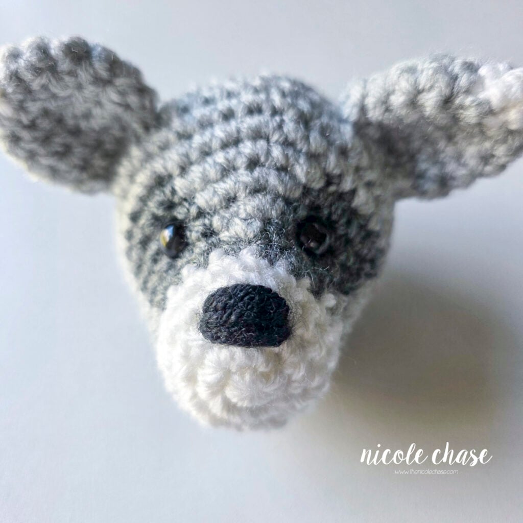 The yarn tails have been secured and hidden inside, completing the crochet raccoon's embroidered nose on the head. 