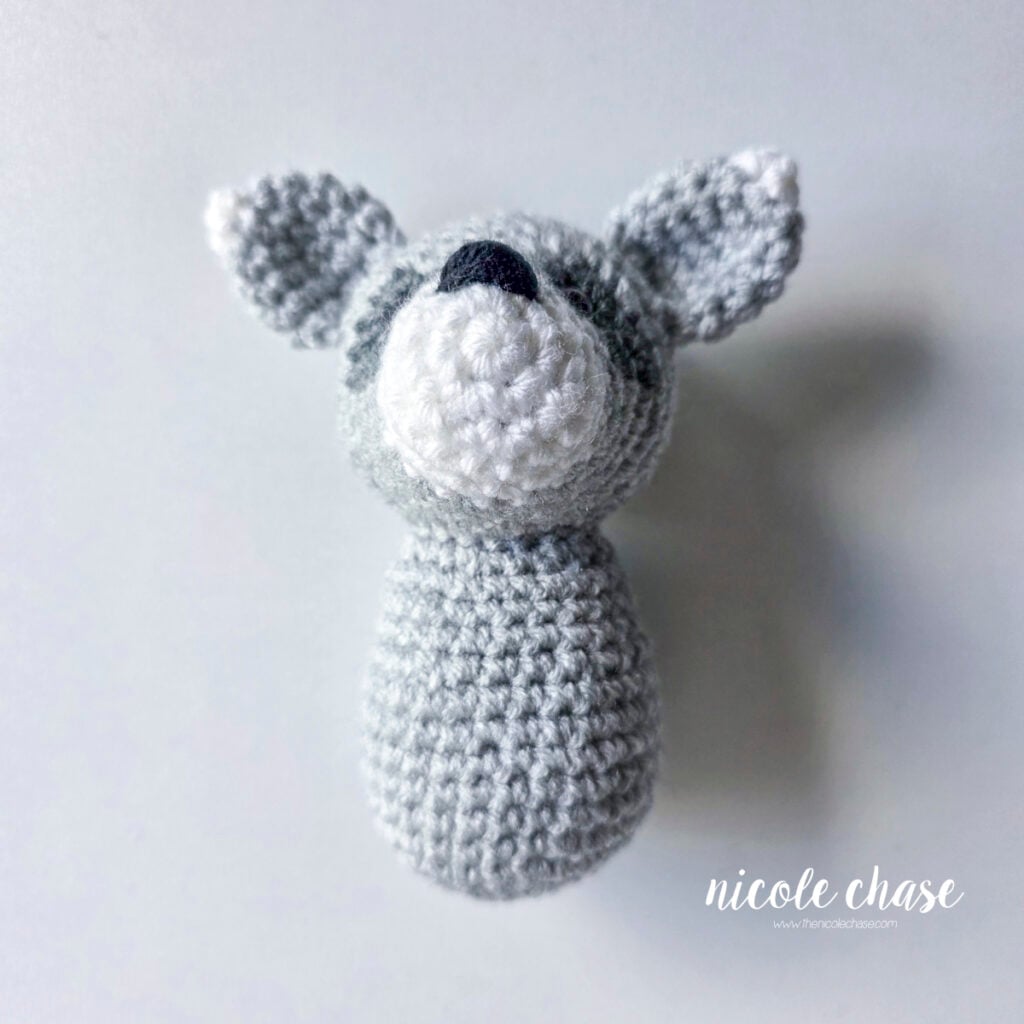 The body of the crochet raccoon has been sewn into place on the bottom of the head. 