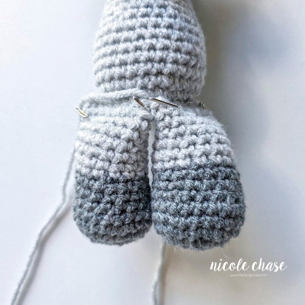 The crochet legs of the raccoon has been pinned into place on the bottom of the body prior to sewing. 