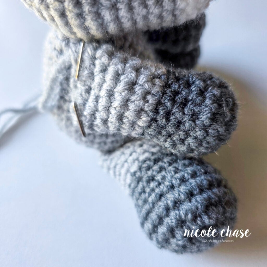The arms of the crochet raccoon have been pinned into place on the side of the body, ready for sewing. 