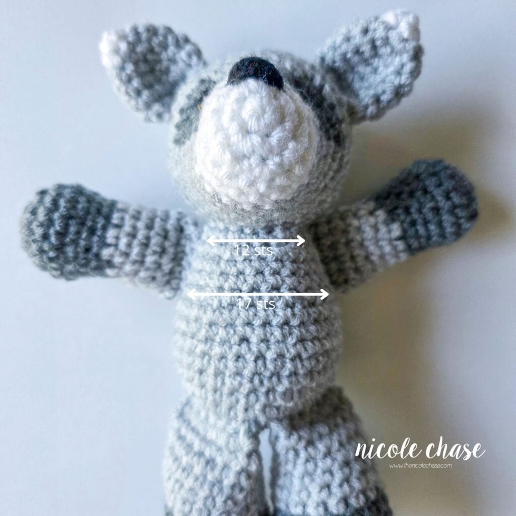 The arms have been sewn into place on the sides of the crochet raccoon body, and a graphic demonstrates the distance between each arm. 