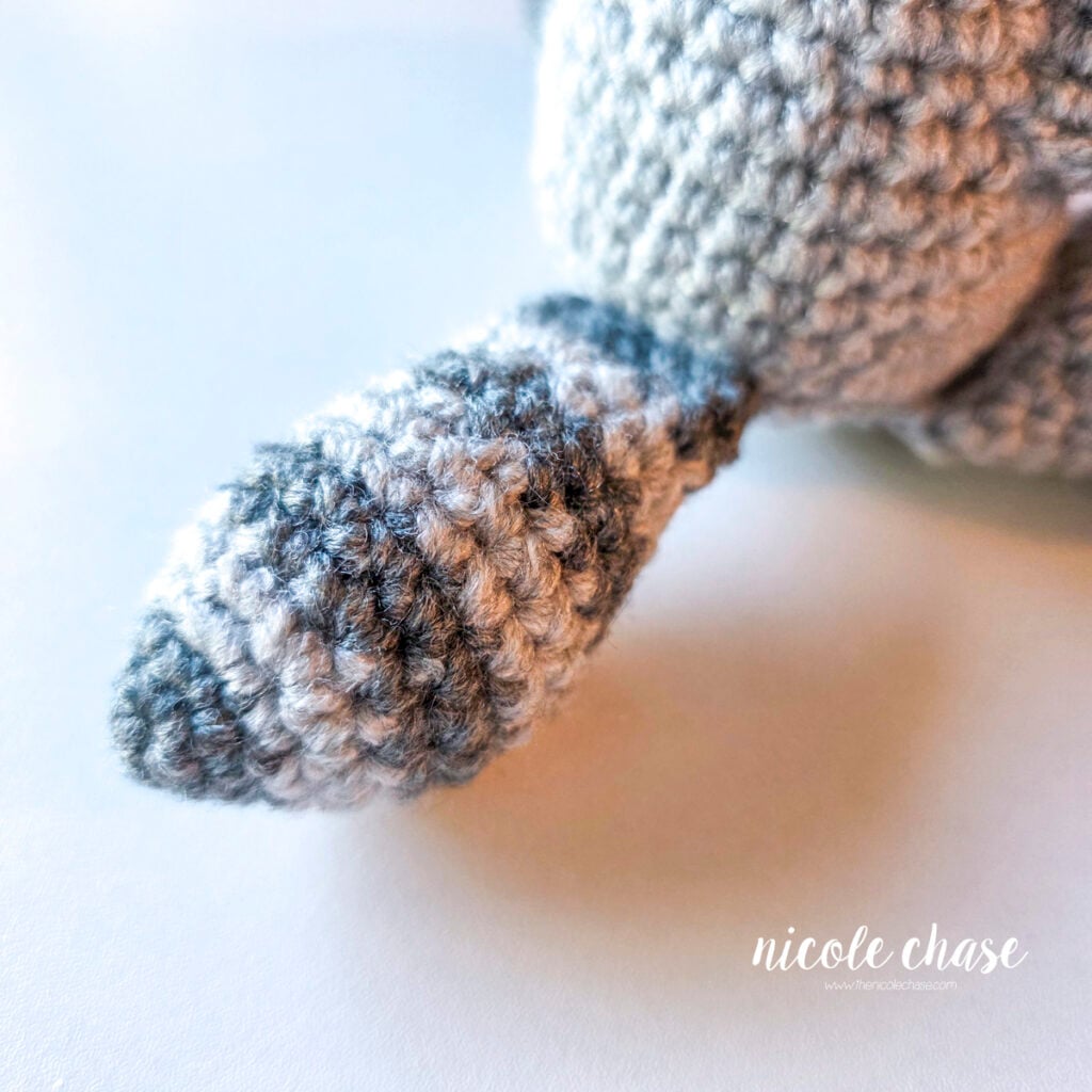 The striped crochet tail of the crochet raccoon has been sewn into place on the back of the body. 