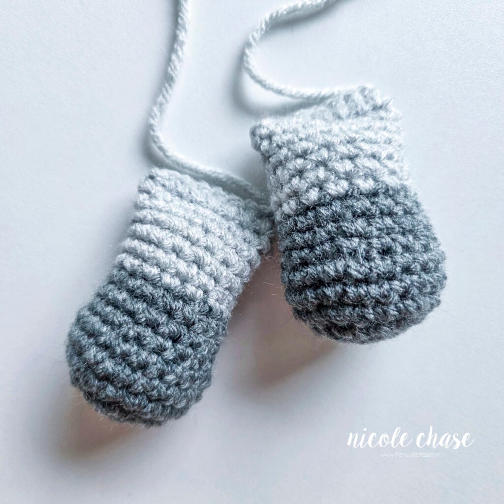 Two finished legs for the raccoon amigurumi made in light gray yarn with dark gray on the base. Filled with stuffing and awaiting assembly. 