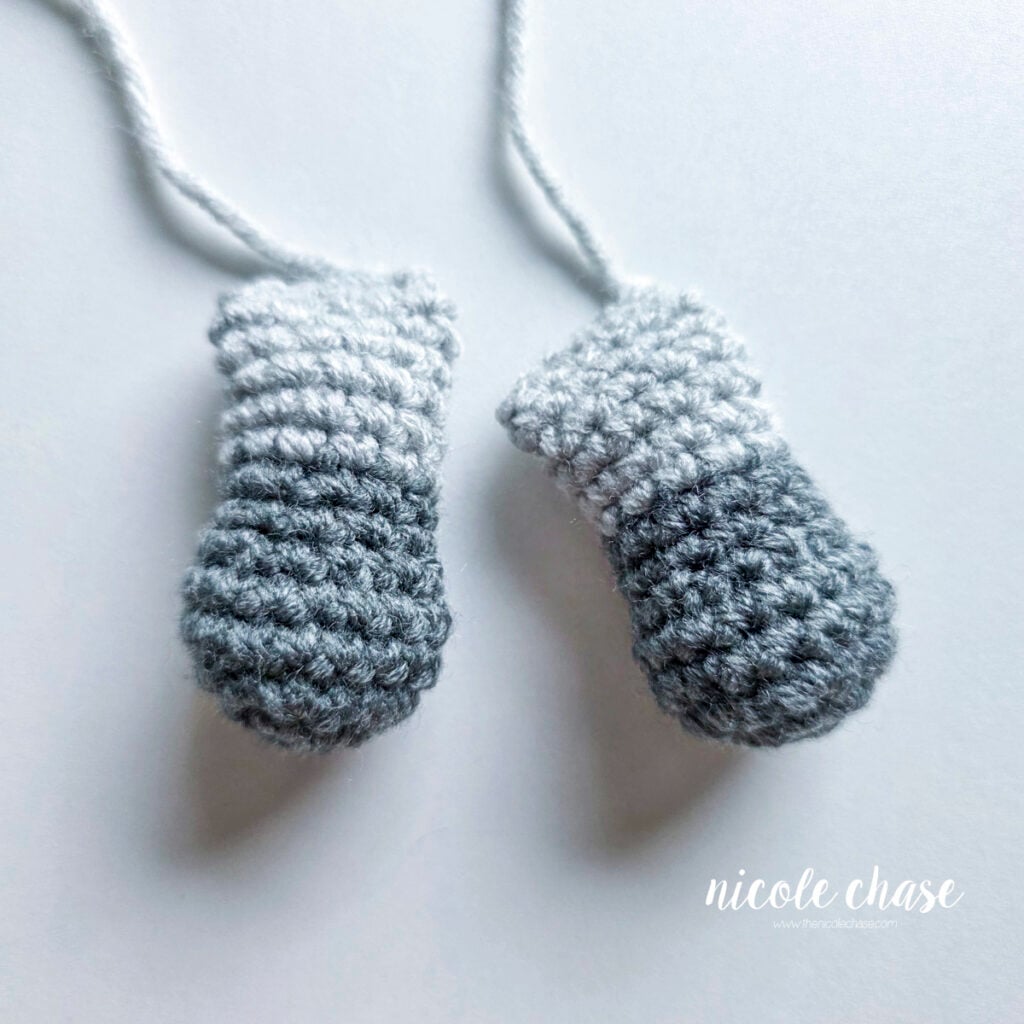 Two crochet arms for the amigurumi raccoon made in light gray and dark gray yarn, filled with stuffing and awaiting assembly. 