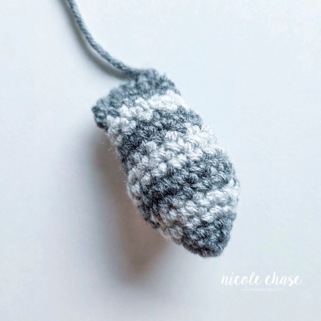 Finished tail for the raccoon crochet pattern shown with dark gray and light gray stripes and filled with stuffing. 