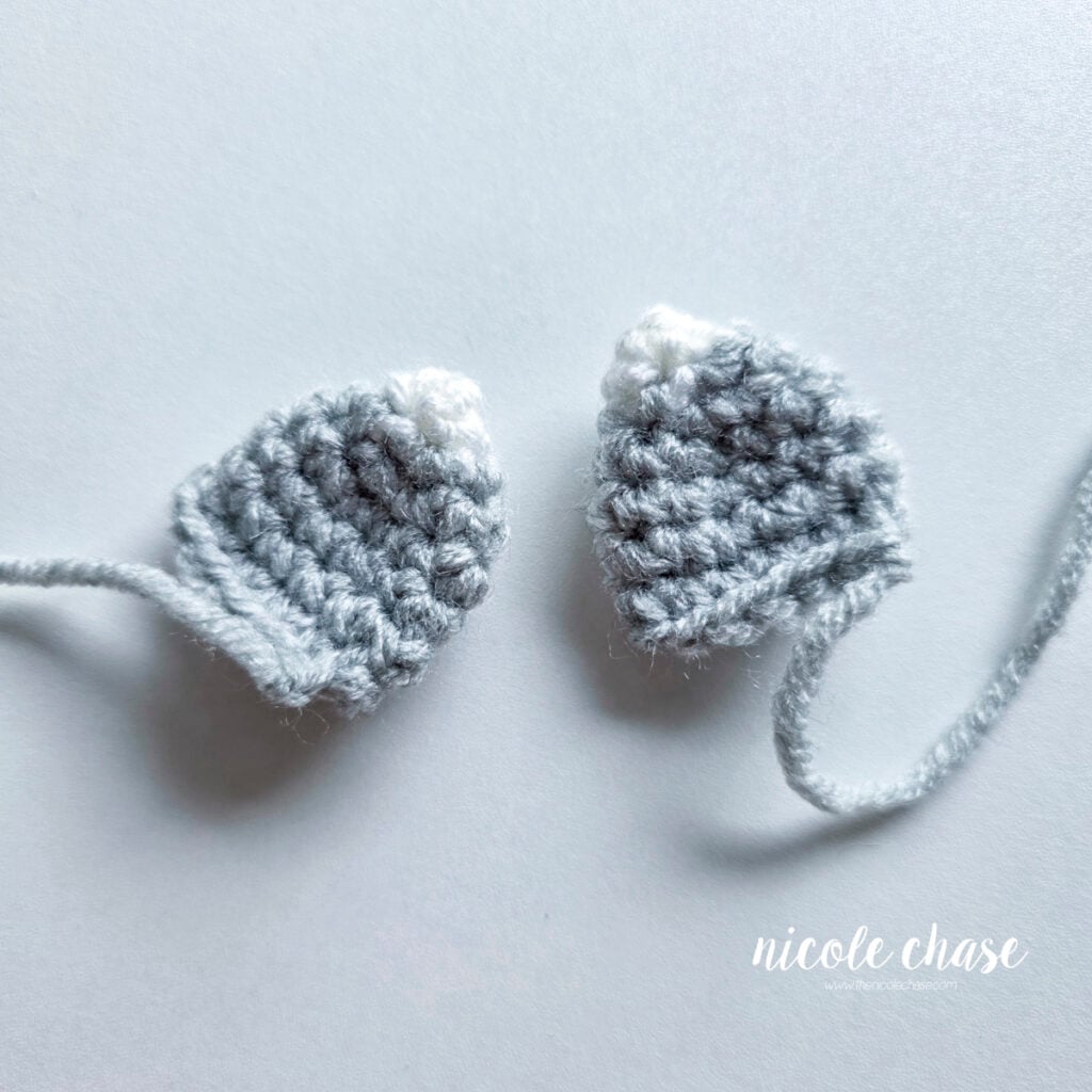 Two finished ears of the crochet raccoon made in light gray yarn with white tips. 