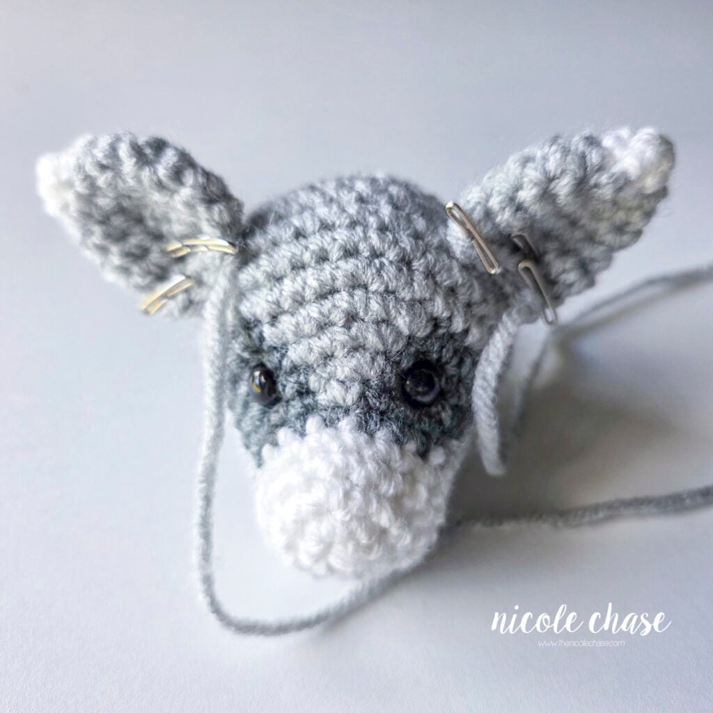 The crochet raccoon ears have been pinned into place on top of the head and are awaiting sewing. 